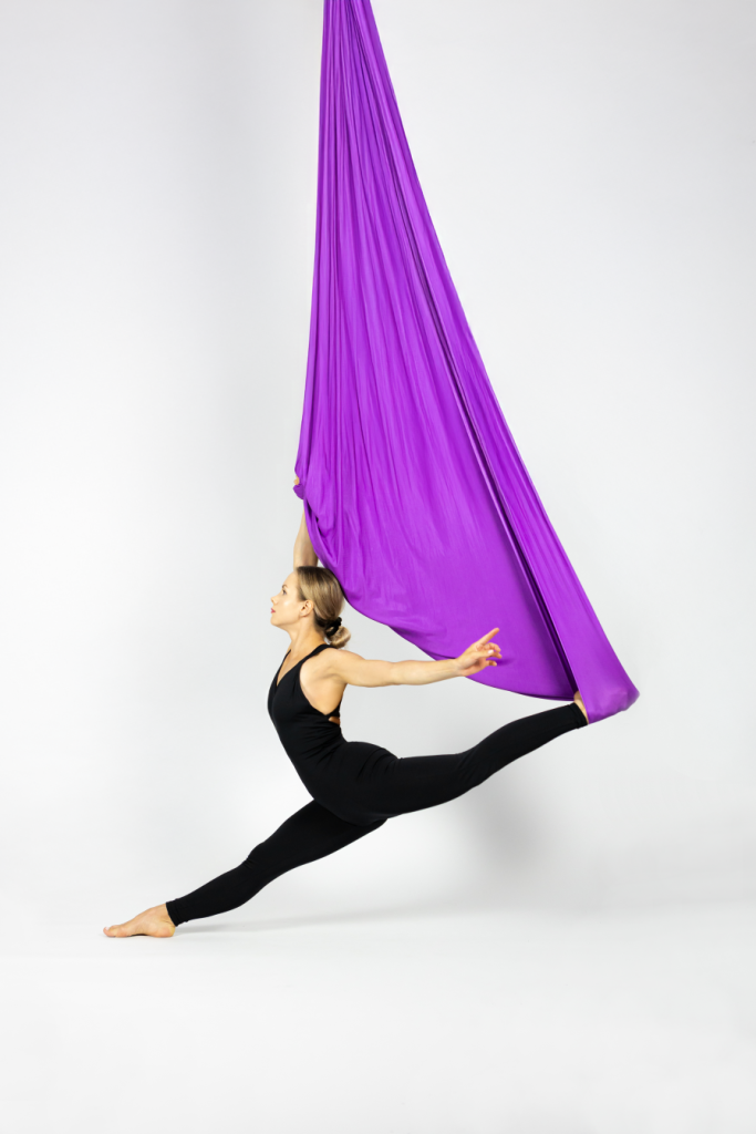 Woman doing splits in purple aerial hammock during aerial stretching class in Krakow
